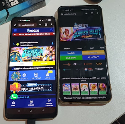 Two smartphones are displayed on a white surface, both showing gambling websites with colorful graphics, text, and various options for logging in and accessing games. The screens are bright and filled with promotional content related to casino and slot games.